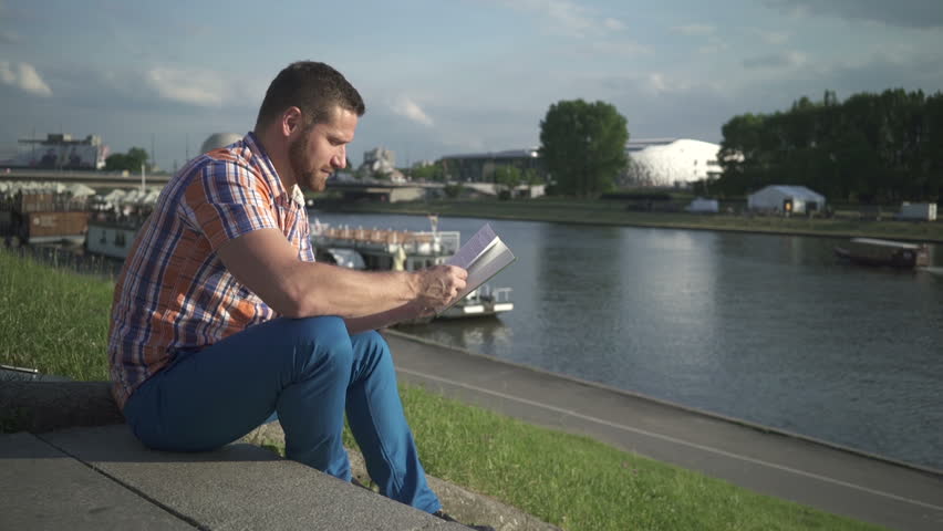 Man reading book on the stairs by the river.