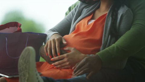Happy mixed ethnicity couple expecting a baby relaxing in the park. Shot on RED Epic.