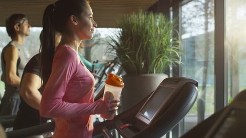 Fit athletic girl is drinking protein shake while exercising on treadmill in sport gym. Shot on RED Cinema Camera in 4K (UHD).