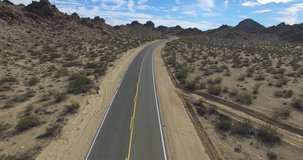 A moving aerial video clip shot at 4K in a desert road and ends passing through some rocky hills.