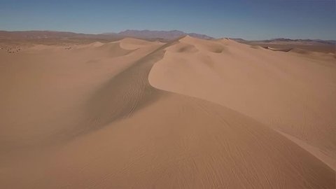An HD drone video footage of flying over sand dunes. Has mountains in the background.