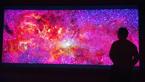 CIRCA 2010s - A man stands before a backlit photo of the universe.