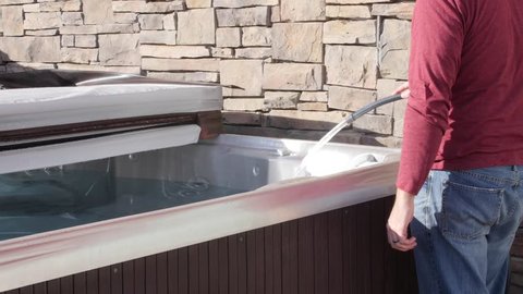 A man prepares to do weekly maintenance on his hot tub and put chemicals in it to clean it.
