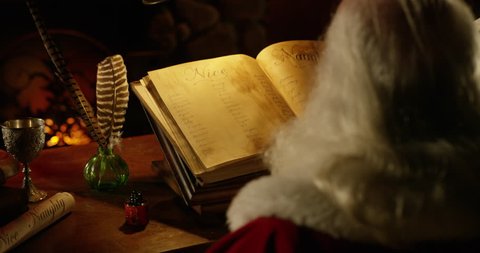 Santa Claus dips quill / pen in ink and camera follows over his head as he writes on Nice list