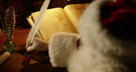 Santa Claus writes in Naughty or Nice book - Dolly in wide to close up over the shoulder, he dips his quill in ink and continues