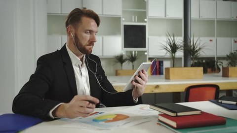 Businessman looks at charts and talking to a tablet. Video UHD 