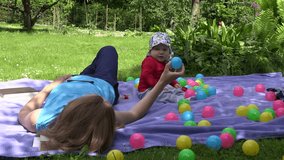 busy mother play with baby girl and talk mobile smart phone lying on mat in green park. 4K UHD video clip.