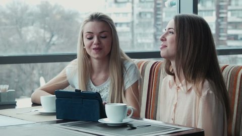The girlfriends speaks in cafe using tablet