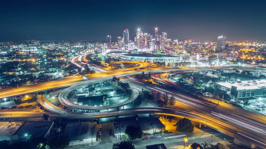 Aerial view of traffic on freeway interchange in downtown Los Angeles skyline at night. 4K UHD timelapse 