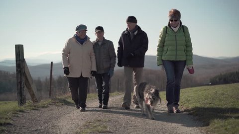 4k footage, active seniors taking dog for a walk on dirt road in hilly countryside
