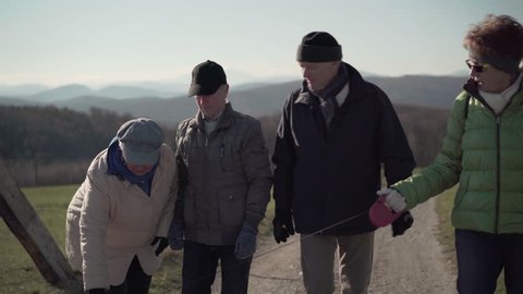 4k footage, medium shot four happy active seniors walking and chatting on sunny winter day without snow in rural landscape
