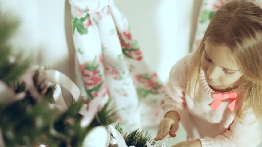 Cute little girl in pink sweater decorates the Christmas tree