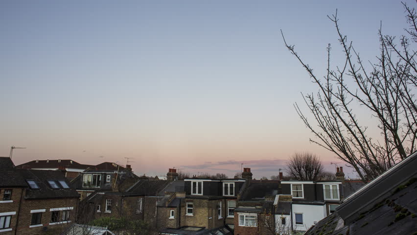 Time lapse view of London cityscape at the sunset, United Kingdom. Beautiful colorful sky and urban silhouette of roofs and suburban houses and apartments .