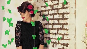 Beautiful brunette girl with roses in hair and clothed in black dress posing for the camera while rounded by green paper butterflies