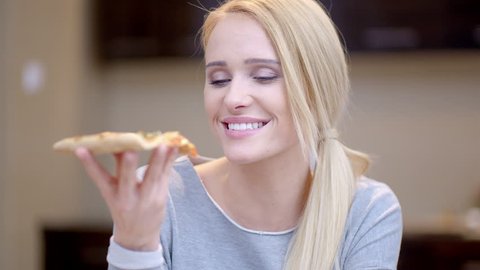 Attractive woman enjoying a slice of pizza biting into it with her eyes close as she savors the aroma and flavor