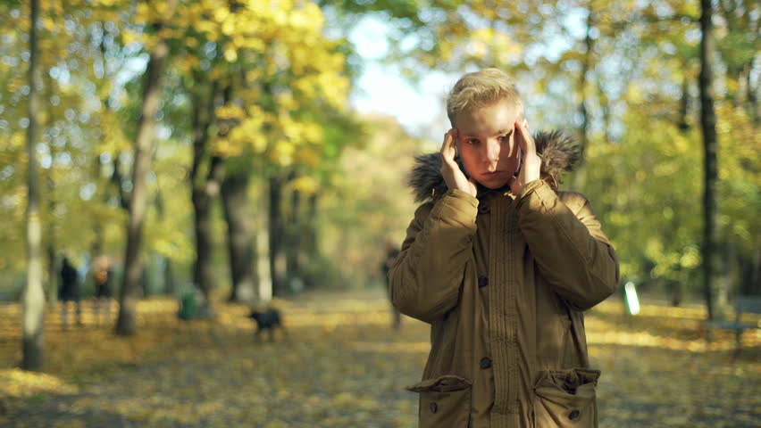 Man standing in the autumnal park and having a headache
