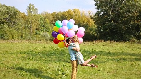 Couple in love are kissing and holding multicolored balloons in beautiful sunset