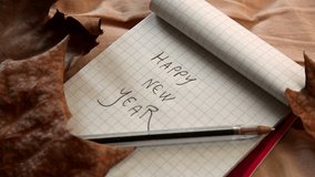 still life of a notebook surrounded by leaves with the wish of happy new year