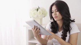happy young asian woman using tablet computer doing video call while relaxing at home