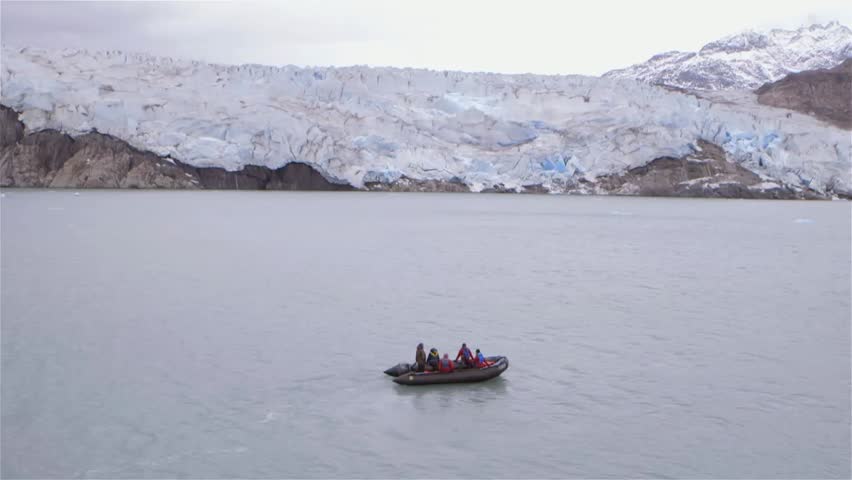Tourists on a zodiac boat tour in Greenland during an expedition with a glacier in the background. (Slow Motion)