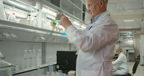 Scientist making chemical reaction and looking at substances in flasks Stockvideo