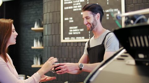 Hipster barista serves coffee and interacts with customers in modern trendy coffee shop cafe