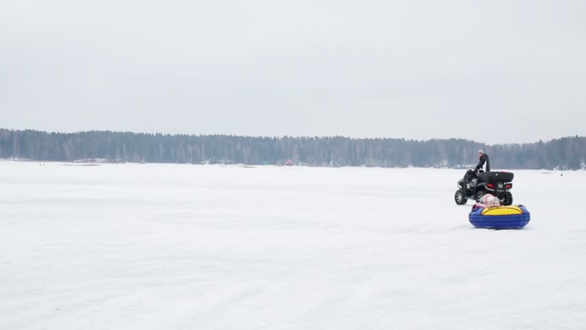 Man on quad bike rolls happy kid on snowy field at winter