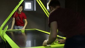 Young man and teen playing air hockey game
