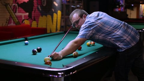 Young man playing pool billiard, takes aim and hits the ball, the ball rolled into the pocket