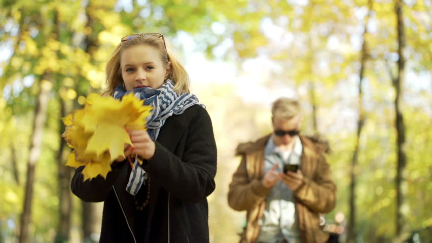 Girl throwing maple leaves and her boyfriend using smartphone
