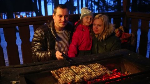 Father, mother and daughter make barbecue with meat at winter night