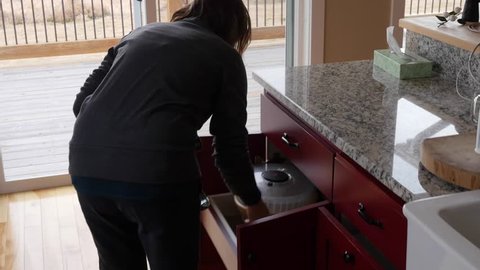A gimbal shot of a woman putting away her clean dishes in the kitchen cupboards