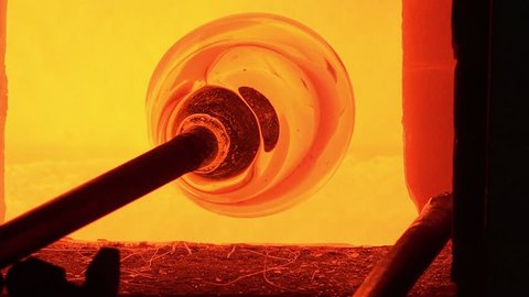Glass-blower working in his workshop/the molten glass is picked with the blowing rod