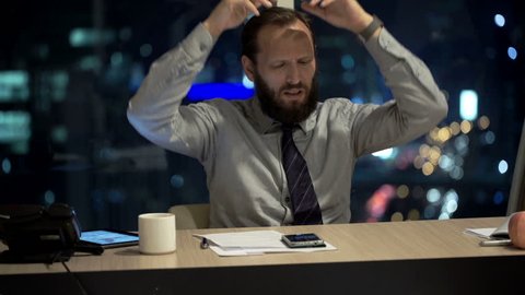 Angry businessman throwing laptop in office at night
