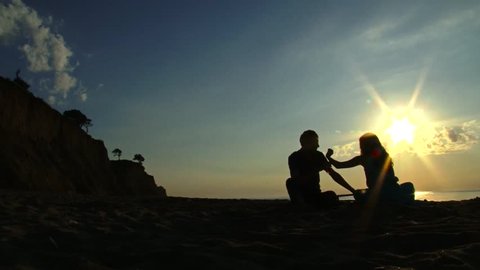 Silhouettes of two lovers seated on the beach (sunrise, sunset) 