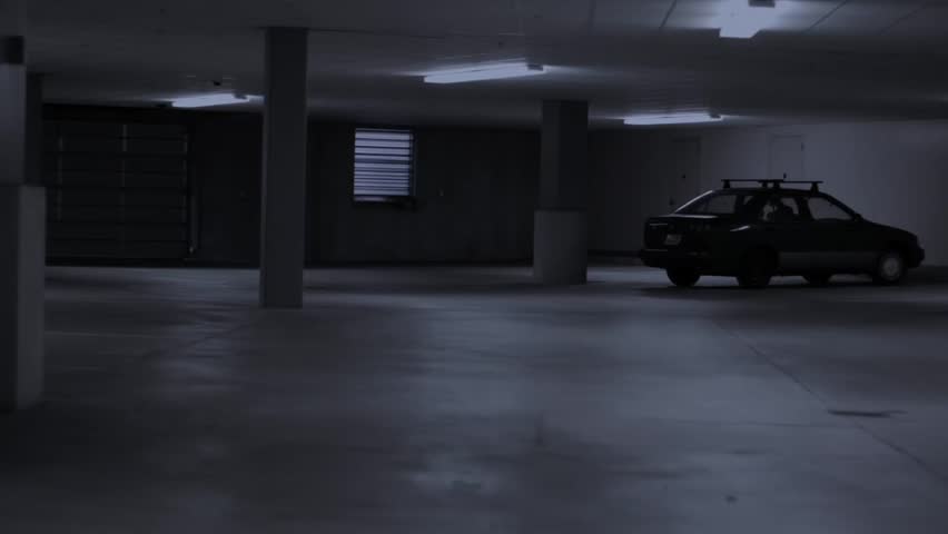 A woman walks through a dark parking garage by herself