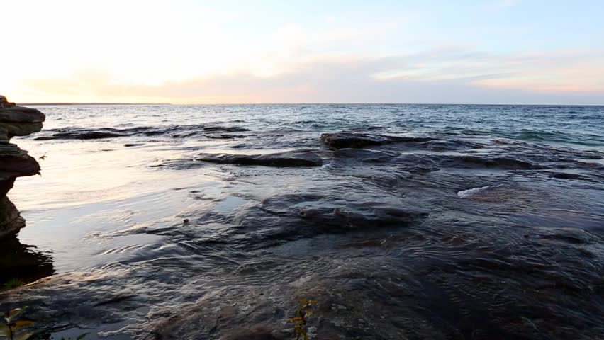 Waves on Lake Superior Shoreline in the Upper Peninsula of Michigan. Under a Lake Superior sunset, waves crash over sandstone rock at Five Mile Point near Christmas Michigan.