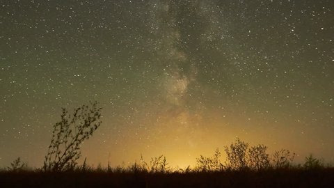 Night sky of stars time-lapse - Milky Way and glow above grass field, star and airliner trails 
