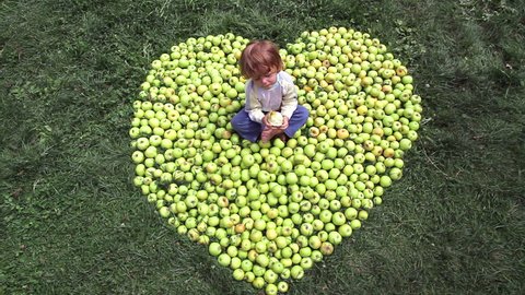 A little boy sits among apples folded into the shape of heart