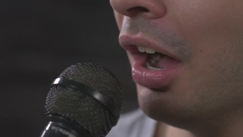 Young man singing in a microphone . Closeup on the mouth.