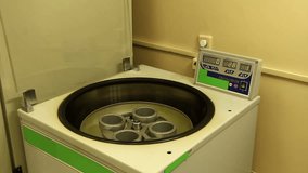 A man in white clothing and gloves loads glassware into centrifuge, closes transparent cover and starts device.  Closed transparent centrifuge cover. No camera movement. 
