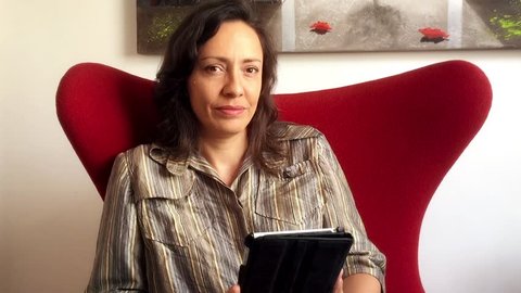 Mature brazilian woman sitting in armchair using tablet computer 