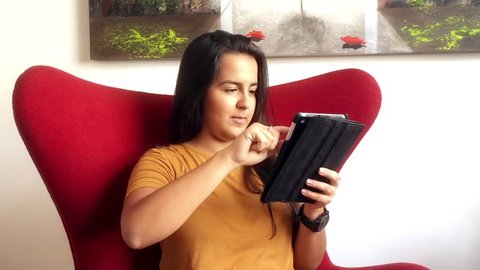 Young brazilian woman sitting in armchair using tablet computer 