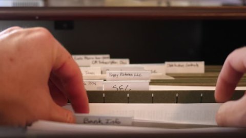 A man working in his home office opens his filing cabinet and looks for a document in a file
