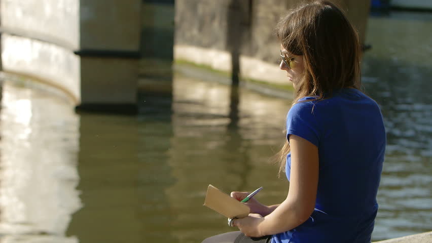 Romantic young woman writing close the river