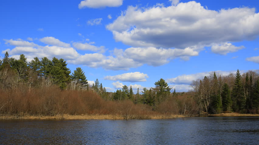 4k Time lapse. White clouds moving through blue sky in spring wind over forest and Oxtongue River in Alqonuin Highlands, Ontario, Canada