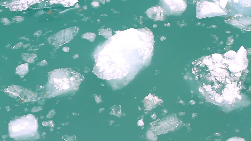 alaskan water with pieces of glacier drift by quickly, aerial view.