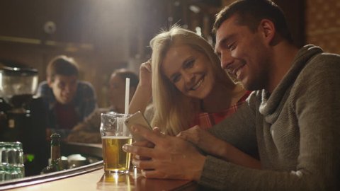 Man and woman laugh while using a smartphone and having a good time in a bar. Shot on RED Cinema Camera in 4K (UHD).