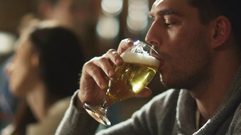 Attractive man is drinking lager beer that was given to him by bartender in a pub. Shot on RED Cinema Camera in 4K (UHD).