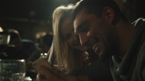 Friends laugh, drink beer and cocktails while having a good time together at a dark bar. Shot on RED Cinema Camera in 4K (UHD).